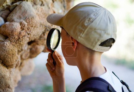 boy with backpack cap and magnifying glass, looking closely at the living creatures that inhabit a rock face