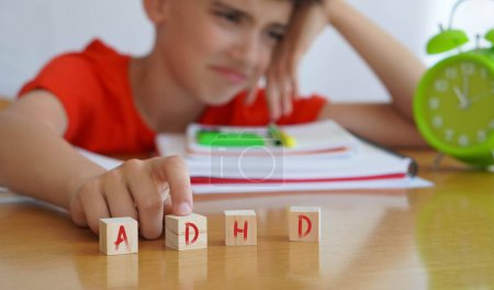 child surrounded by books and notebooks frustrated, with the acronym ADHD, represents the disease Attention Deficit Disorder and the difficulties it entails in school life.