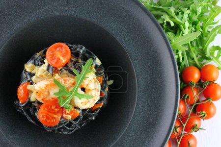 Foto de Espaguetis negros. Pasta de mariscos negros en plato blanco sobre fondo negro con espacio para copiar - Imagen libre de derechos