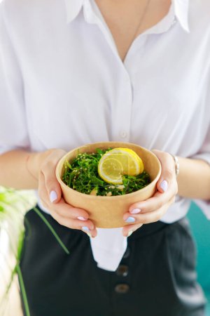 Téléchargez les photos : Salade Hiyashi Wakame dans un récipient de livraison de nourriture Kraft dans des mains féminines, salade Chuka, - en image libre de droit
