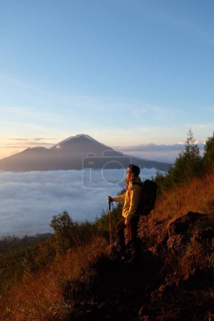 Photo for Skyward Summit, Asian Model on Mount Batur, Carrying Hiking Gear amidst Cloud Ocean - Royalty Free Image