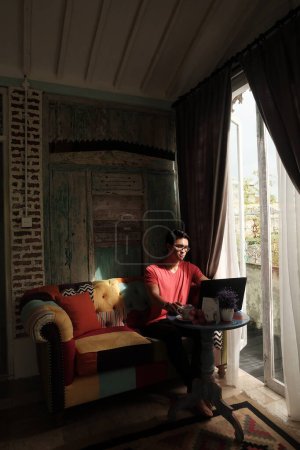 Photo for Villa Relaxation, Asian Model Working on Laptop, Basking in Sunlit Comfort - Royalty Free Image
