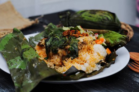 Foto de Nasi bakar (indonesio para "arroz quemado o a la parrilla") se refiere al arroz al vapor sazonado con especias e ingredientes y envuelto en hoja de plátano asegurada con lidi semat ( - Imagen libre de derechos