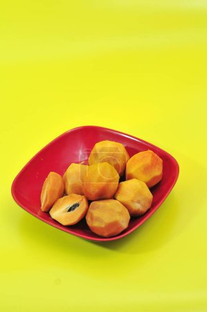 Photo for Sapodilla fruit that has been peeled on a maroon plate and a yellow background - Royalty Free Image