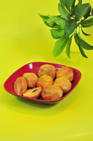 Téléchargez les photos : Fruits de sapodilla qui a été pelé sur une assiette de marron et un fond jaune - en image libre de droit