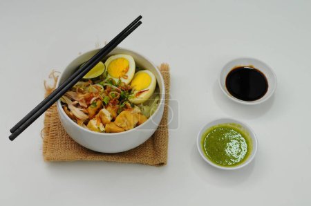 Soto comes from Chinese food in the Hokkian dialect Cau do, Jao To, or Chau Tu, which means 'grass' or 'spice offal'. served on white bowl with tofu, chicken and boiled egg