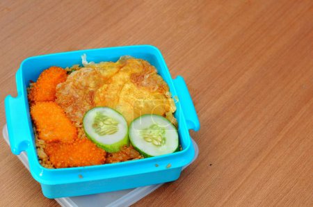 Téléchargez les photos : Boîte à lunch contenant riz frit, pépites et nouilles frites, sur une table en bois - en image libre de droit