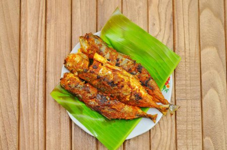 Ikan Bakar or Grilled fish with indonesian spices served on banana leaf and isolated wood background.