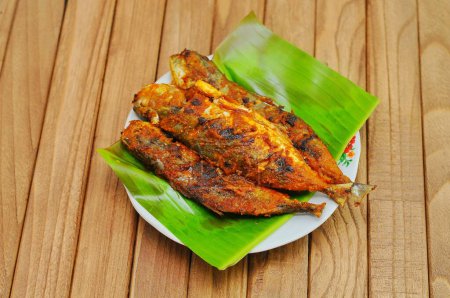 Téléchargez les photos : Ikan Bakar ou poisson grillé aux épices indonésiennes servi sur feuille de banane et fond de bois isolé. - en image libre de droit