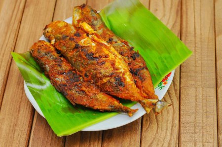 Photo for Ikan Bakar or Grilled fish with indonesian spices served on banana leaf and isolated wood background. - Royalty Free Image