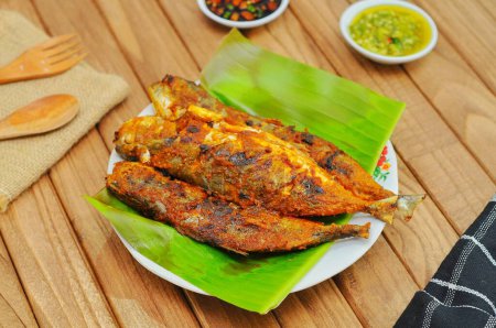 Ikan Bakar ou poisson grillé aux épices indonésiennes servi sur feuille de banane et fond de bois isolé.