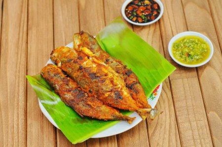 Ikan Bakar oder Gegrillter Fisch mit indonesischen Gewürzen auf Bananenblatt und isoliertem Holzhintergrund.