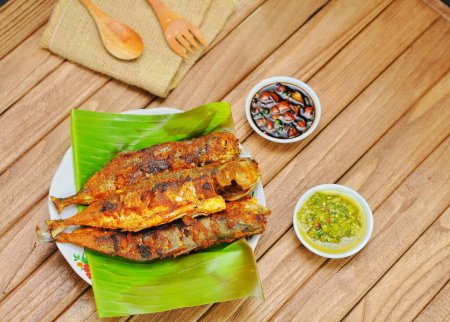 Ikan Bakar ou poisson grillé aux épices indonésiennes servi sur feuille de banane et fond de bois isolé.