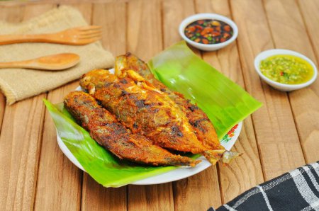 Ikan Bakar or Grilled fish with indonesian spices served on banana leaf and isolated wood background.