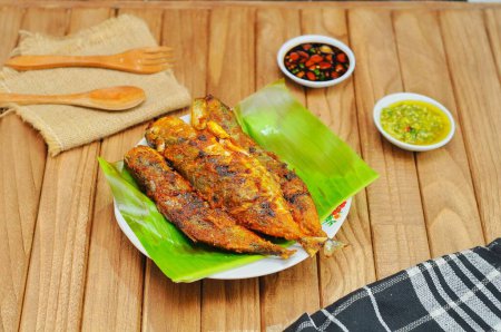 Téléchargez les photos : Ikan Bakar ou poisson grillé aux épices indonésiennes servi sur feuille de banane et fond de bois isolé. - en image libre de droit