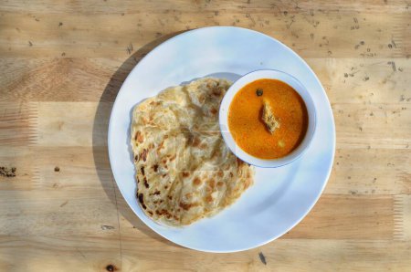 Photo for Roti canai with goat curry on a white plate and wooden table - Royalty Free Image