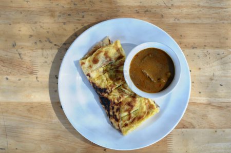 roti canai with goat curry on a white plate and wooden table