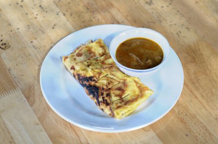 roti canai with goat curry on a white plate and wooden table