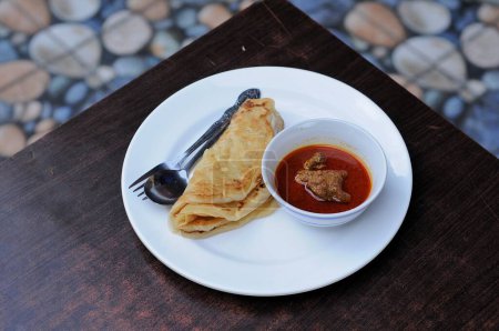 roti canai au curry de chèvre sur une assiette blanche et une table en bois