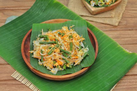 Foto de Enfoque selectivo Urap Sayur es comida tradicional indonesia. un plato de ensalada de verduras al vapor varias mezcladas con sazonado y especiado, servido en hoja de plátano y plato de madera - Imagen libre de derechos