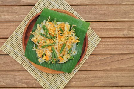 Téléchargez les photos : Concentration sélective Urap Sayur est une cuisine traditionnelle indonésienne. un plat de salade de légumes cuits à la vapeur mélangés avec assaisonné et épicé, servi sur feuille de banane et assiette en bois - en image libre de droit