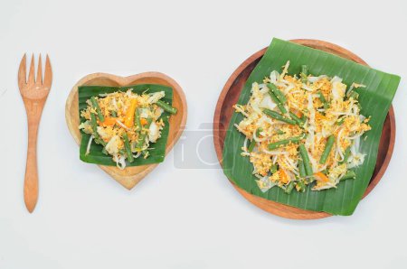 Foto de Enfoque selectivo Urap Sayur es comida tradicional indonesia. un plato de ensalada de verduras al vapor varias mezcladas con sazonado y especiado, servido en hoja de plátano y plato de madera - Imagen libre de derechos