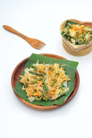 Téléchargez les photos : Concentration sélective Urap Sayur est une cuisine traditionnelle indonésienne. un plat de salade de légumes cuits à la vapeur mélangés avec assaisonné et épicé, servi sur feuille de banane et assiette en bois - en image libre de droit