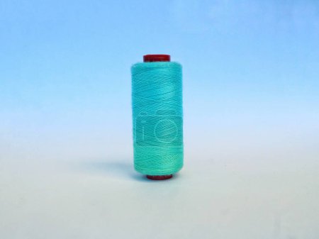 A spool of thread filled with turquoise green in a standing position