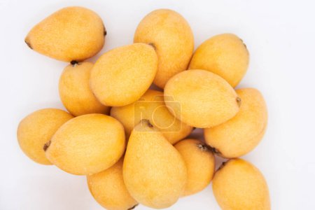 Looking down at a pile of ripe loquats on a white background