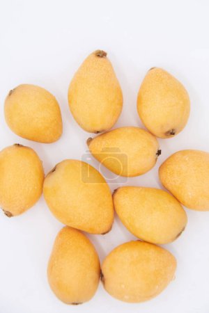 Looking down at a pile of ripe loquats on a white background