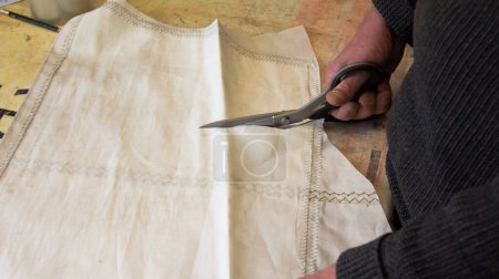 Photo for The tailor cuts out a piece of a white sail with a scissors to process it further. - Royalty Free Image