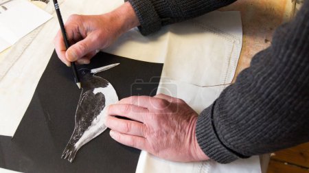 Photo for A tailor traces a stencil of a seahorse on a red canvas with his hand and a pencil - Royalty Free Image