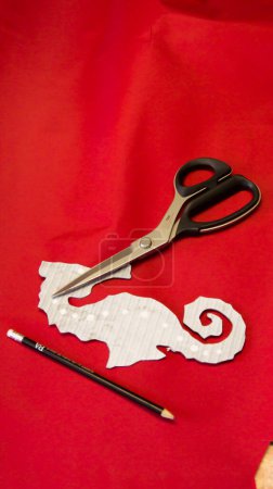 Téléchargez les photos : Tissu toile rouge avec un motif hippocampe d'un ciseau et un crayon, le tailleur travaillera sur cette table - en image libre de droit