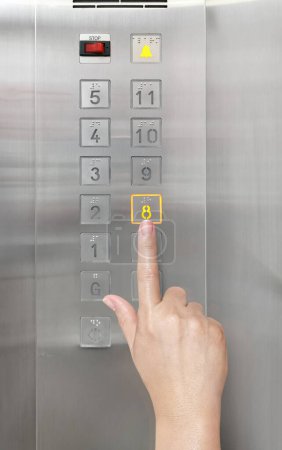 La mano de una mujer está usando su dedo para presionar el botón del ascensor.