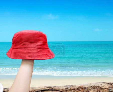 sombrero de cubo rojo en la mano con fondo de playa