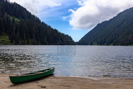 A canoe sits on the sandy shore of a mountain lake surrounded by forest. It invites you to go exploring on the cool water.