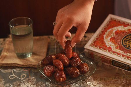 Photo for Fast breaking meal or iftar dish with muslim woman hands praying to Allah. Dates with a glass of mineral water on the table.Traditional Ramadan, fast breaking meal. Indonesia-March 13,2024 - Royalty Free Image