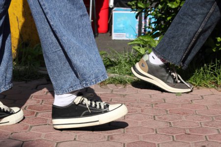 Photo for Cropped section people legs wearing jeans and sneakers, walking by paving stones - Royalty Free Image