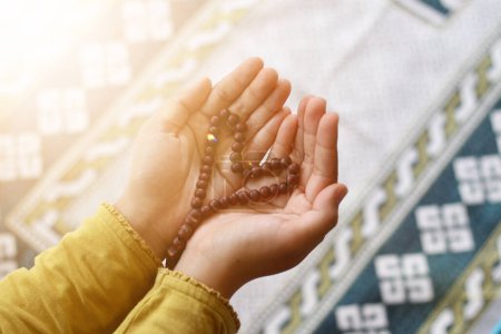 Téléchargez les photos : Les mains priantes de la femme musulmane face à la fenêtre avec la lumière du coucher du soleil par la fenêtre. Concept de kareem Ramadan - en image libre de droit