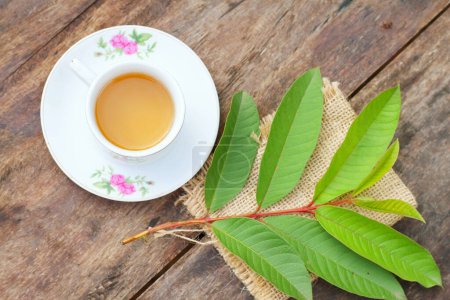 Téléchargez les photos : Daun jambu biji ou goyave laisse le thé dans une tasse blanche sur une table en bois, boisson à base de plantes pour la diarrhée et le cholestérol - en image libre de droit