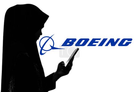 Foto de Indonesia - 28 de marzo de 2024: Mujer sosteniendo un teléfono inteligente frente a una pantalla grande con el logotipo de la compañía Boeing en el fondo. - Imagen libre de derechos
