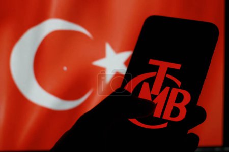 Foto de Indonesia - 30 de marzo de 2024: Banco Central de Turkiye, Trkiye Cumhuriyet Merkez Bankas, TCMB, visualizado en la pantalla del teléfono inteligente Con bandera de Turkiye en segundo plano. - Imagen libre de derechos
