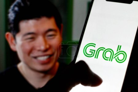 Photo for Indonesia - April 2,2024: Grab logo is displayed on a smartphone screen With CEO Anthony Tan in background. - Royalty Free Image