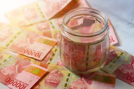 Téléchargez les photos : Indonésie - 7 avril 2024 : Le concept d "épargne pour la comptabilité financière consiste à placer des billets indonésiens dans une coupure de 100 000 roupies dans un bocal en verre. - en image libre de droit