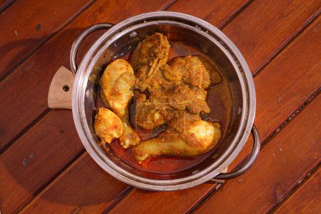 Ayam bumbu kuning or chiken curry served in bowl on woodle table.