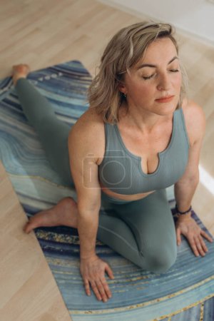 Téléchargez les photos : Une femme de 50 ans fait du yoga à la maison. Photo de haute qualité - en image libre de droit