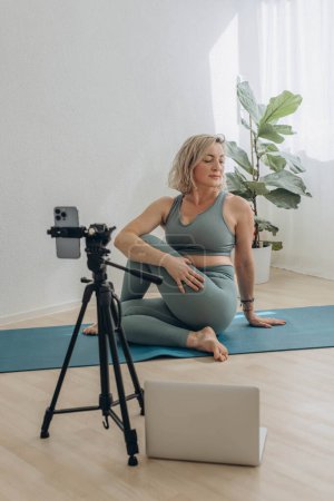 Téléchargez les photos : Une femme de 50 ans qui fait du yoga en ligne à la maison. Photo de haute qualité - en image libre de droit