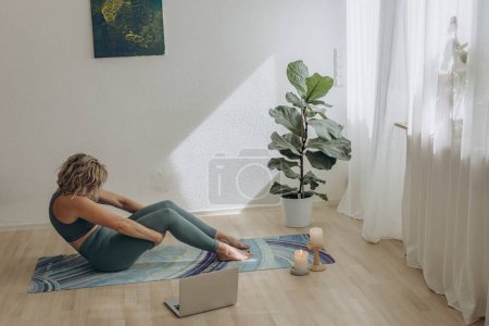 Téléchargez les photos : Une femme de 50 ans qui fait du yoga en ligne à la maison. Photo de haute qualité - en image libre de droit