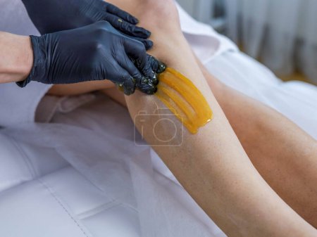 Woman cosmetologist performs sugaring peeling on her legs. High quality photo