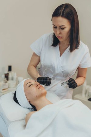 Téléchargez les photos : Cosmetologue esthéticienne effectue un traitement de la peau et de rajeunissement. Photo de haute qualité - en image libre de droit